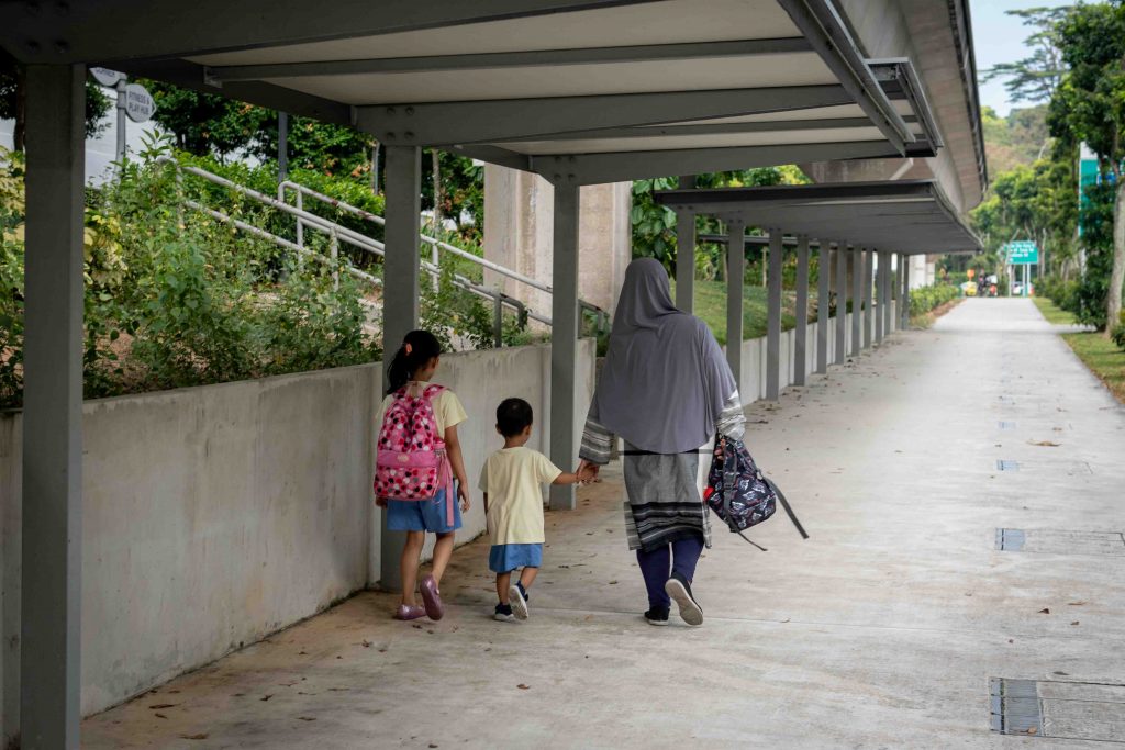 Image of a guardian walking with two children, seemingly of primary school age.