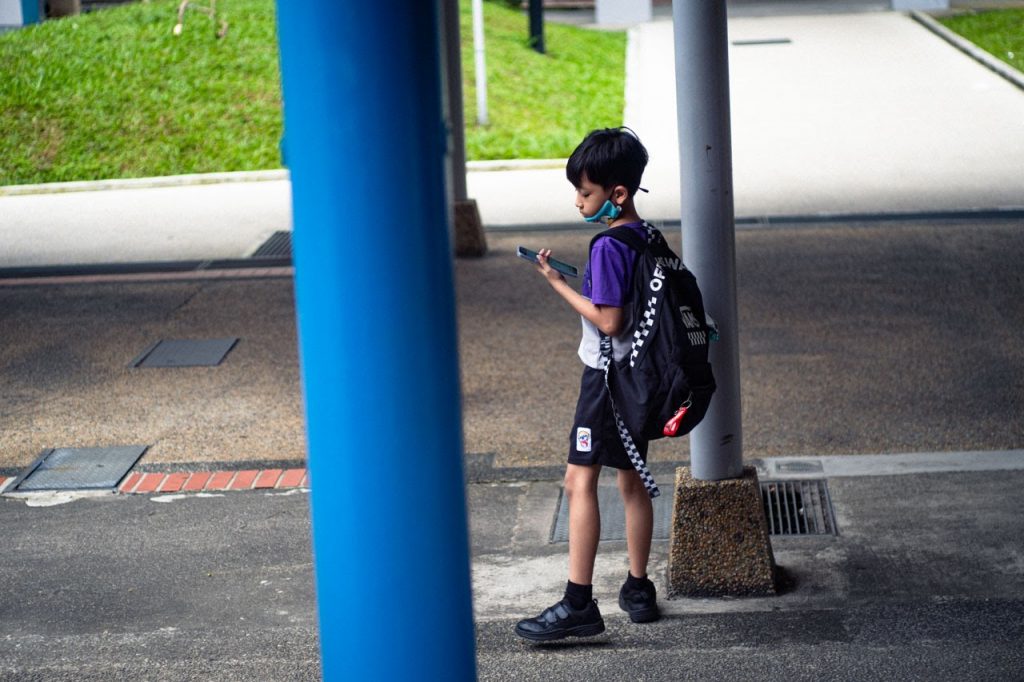 Image of a primary school child with a school bag, looking at his phone. 